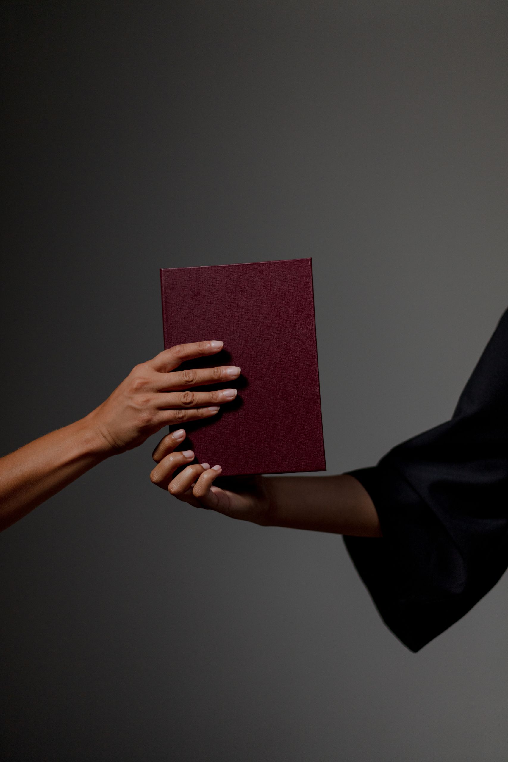 Close-up of two hands exchanging a diploma against a gray background, symbolizing graduation.