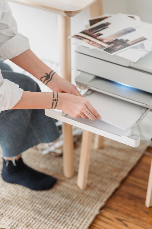 From above of crop anonymous female photographer with tattoo preparing paper for printing photos at home